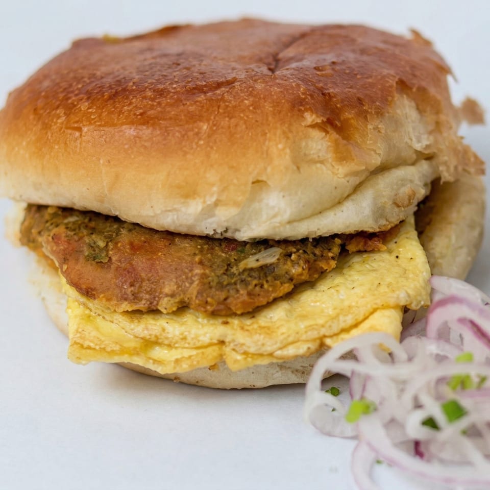 Close-up of a burger with a golden bun, omelet, and patty, served with sliced red onions.
