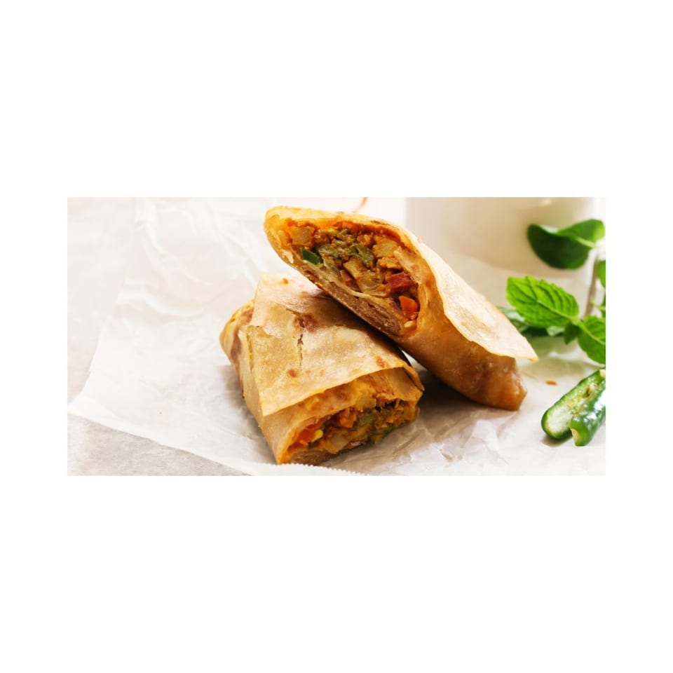 Two golden-brown spring rolls, one cut in half to reveal a savory filling, on white parchment paper.